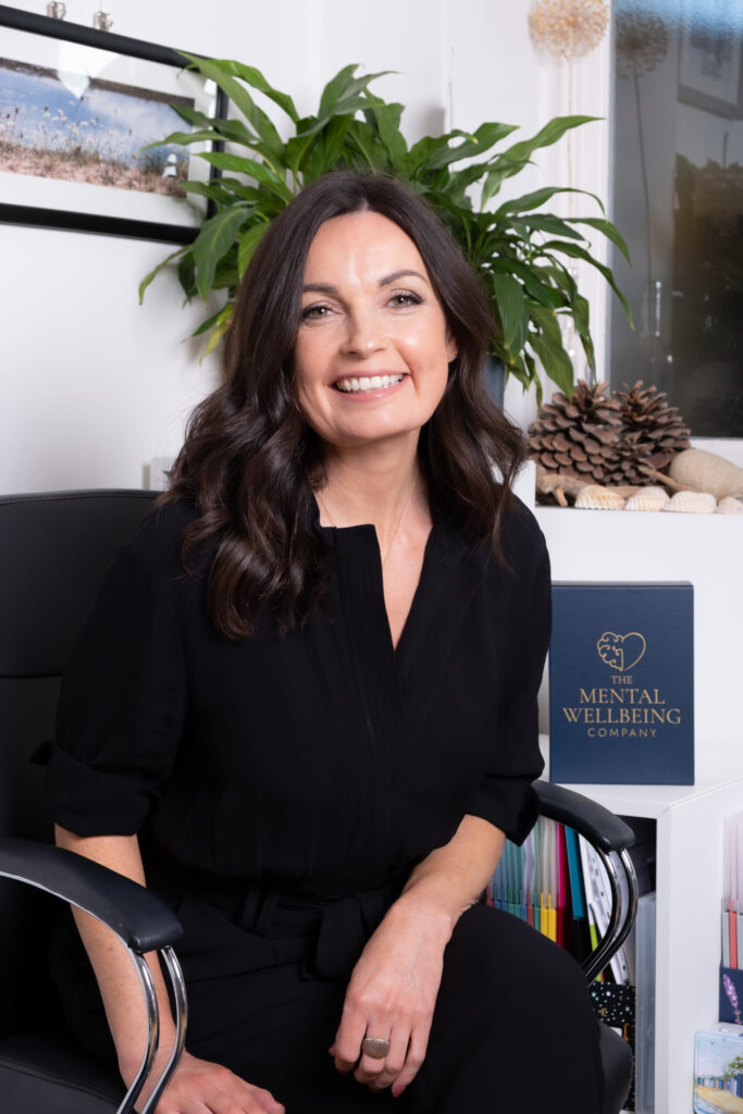 Ruth sitting at a desk, in in dark professional attire, smiling happily.