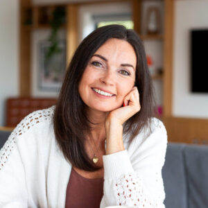 Portrait photo of Ruth looking at the viewer; she has a kind and reassuring smile, her head tilted slightly to the viewer's right and resting upon her part-closed hand.