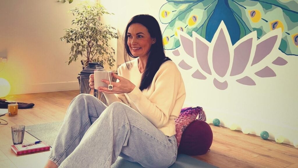 Ruth sitting on a mat with a cup of tea, looking relaxed and happy.